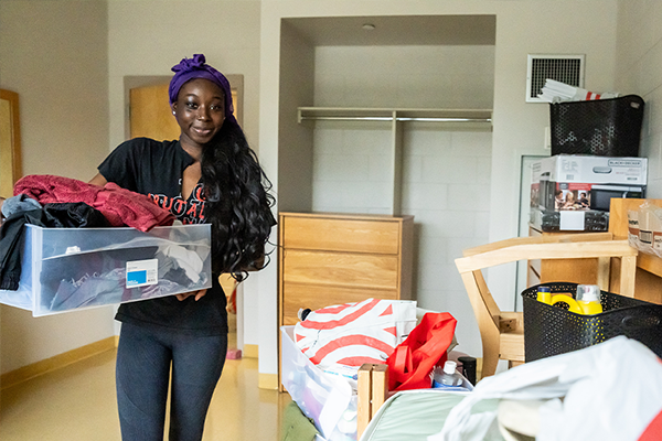 Image of a female student holding a box while moving into the residence halls.