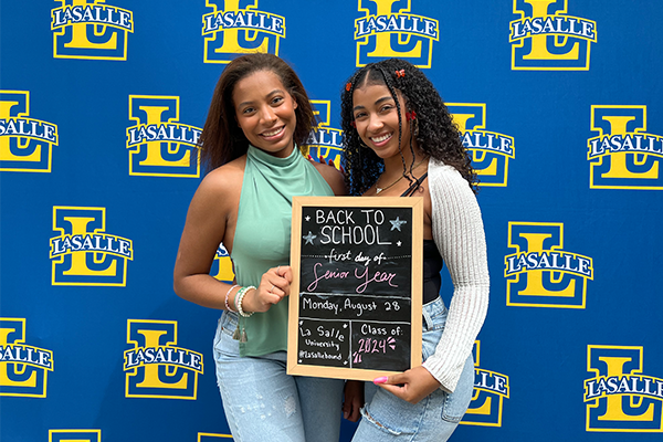 Image of two female students posing with a chalkboard that says "Back to School."