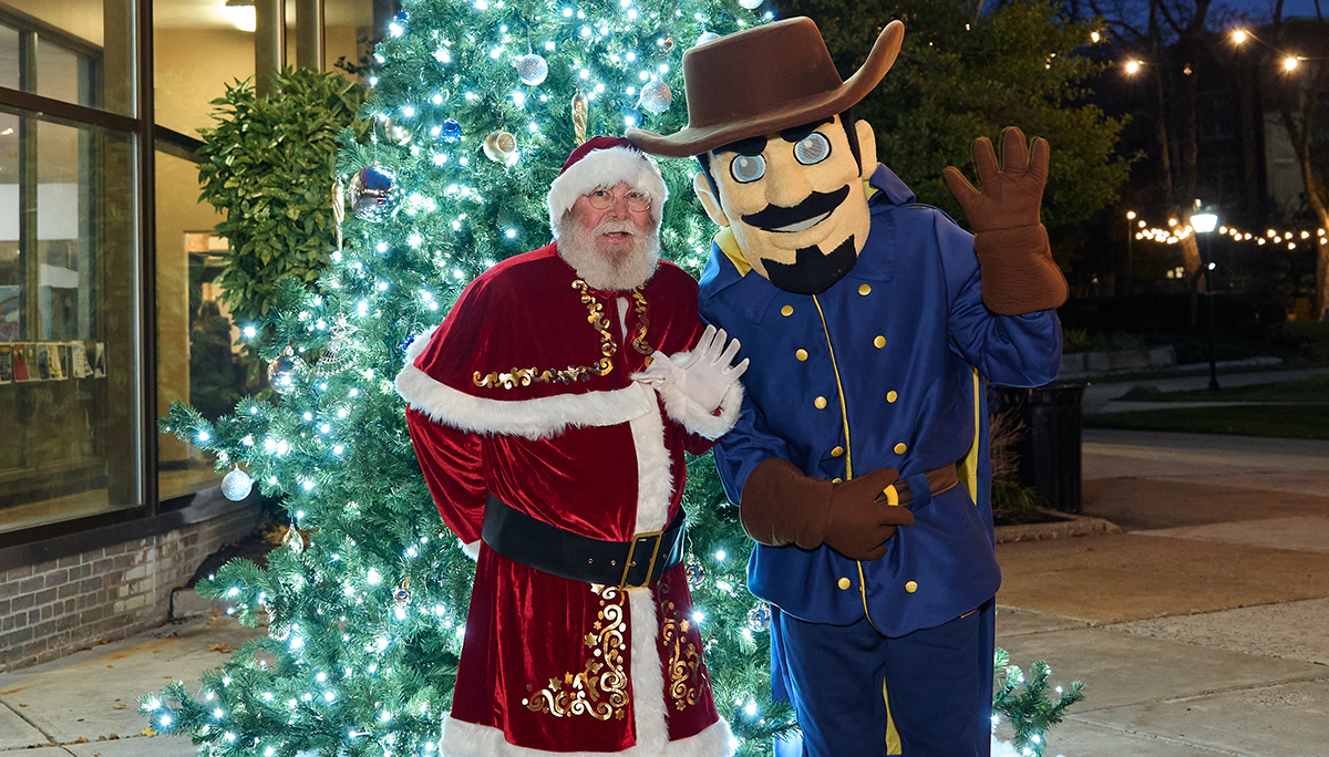 Santa Claus and the Explorer mascot posing in front of the Christmas tree.