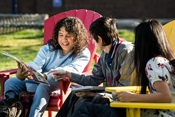 Image of students looking at a notebook while sitting in chairs on the Hansen Quad.