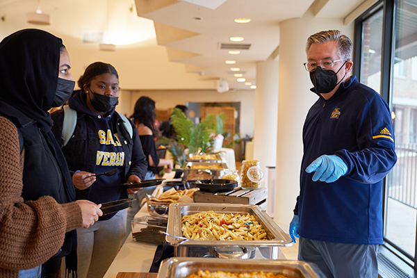 Interim President Tim O’Shaughnessy, ’85, serving food to two students.