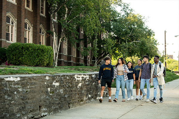 A group of students walking on the sidewalk adjacent to College Hall.